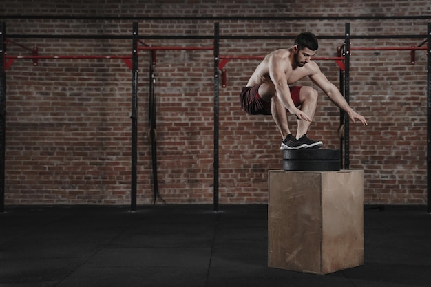 Młody crossfit sportowiec skaczący na siłowni Mężczyzna ćwiczący trening funkcjonalny Miejsce na tekst