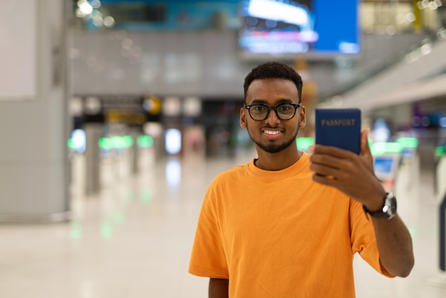 Młody czarny człowiek gotowy do podróży na lotnisku i pokazując paszport