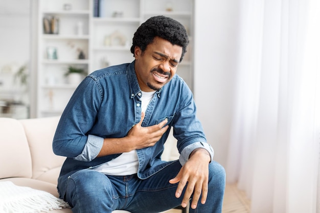 Młody czarny mężczyzna cierpiący na ból klatki piersiowej w salonie