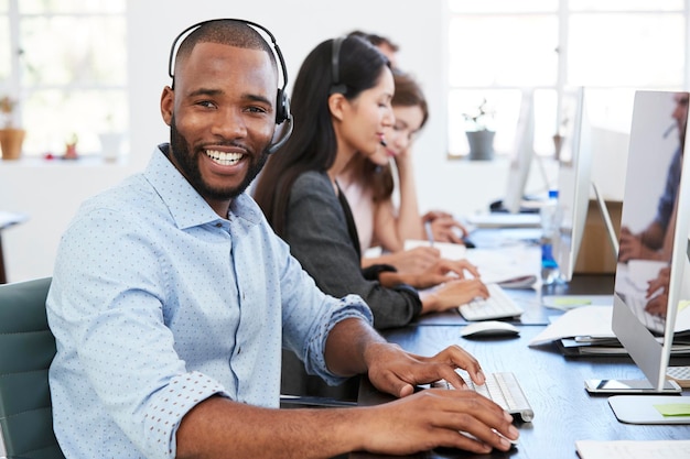 Młody czarny mężczyzna z zestawem słuchawkowym uśmiechający się do kamery w biurze