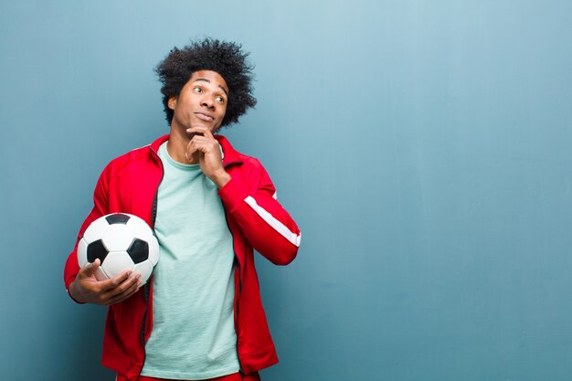 Młody czarny sportowiec z piłką nożną o ścianę niebieski nieczysty