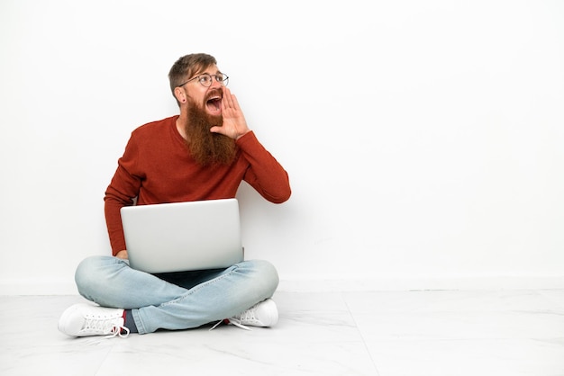 Młody czerwonawo-kaukaski mężczyzna z laptopem na białym tle krzyczy z szeroko otwartymi ustami