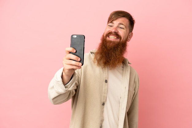 Młody czerwonawy kaukaski mężczyzna na różowym tle robi selfie