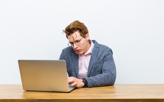 Młody czerwony kierowniczy biznesmen pracuje w jego biurku z laptopem