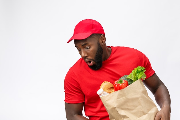 Młody człowiek Afroamerykanin, trzymając w rękach pakiet spożywczy z szokującą twarzą.