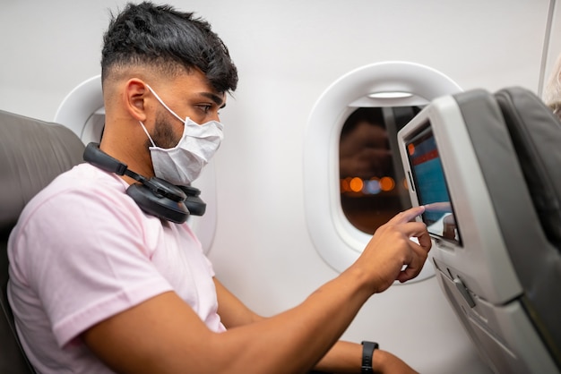 Młody człowiek Ameryki Łacińskiej w ochronnej masce na twarz, podróżujący samolotem