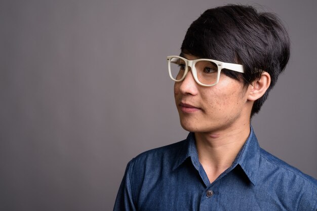Młody człowiek azjatyckich w okularach patrząc mądrze na szarej ścianie
