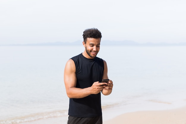 Młody człowiek biegacz wiadomości z komórki inteligentny telefon na plaży