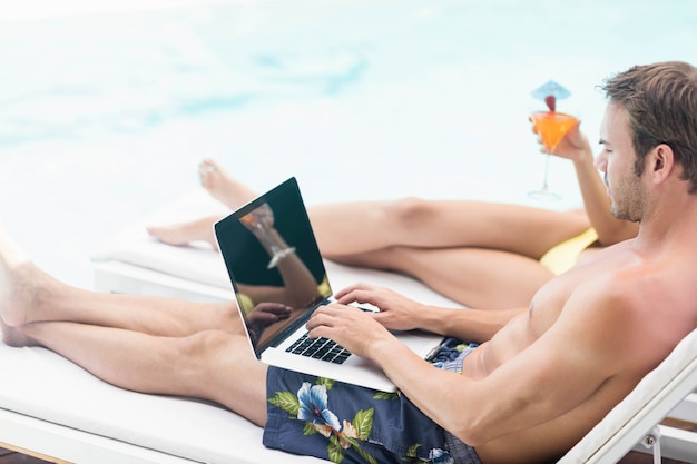 Młody człowiek blisko pływackiego basenu używać laptop