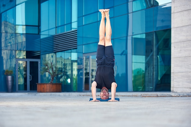 Młody człowiek ćwiczy asana jogi na głowie Sirsasana stanowią na zewnątrz