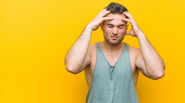 Zdjęcie młody człowiek fitness o żółtą ścianę, dotykając świątyń i mając ból głowy.