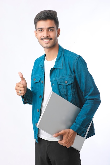 Młody człowiek indyjski trzyma laptopa w ręku na białym tle.