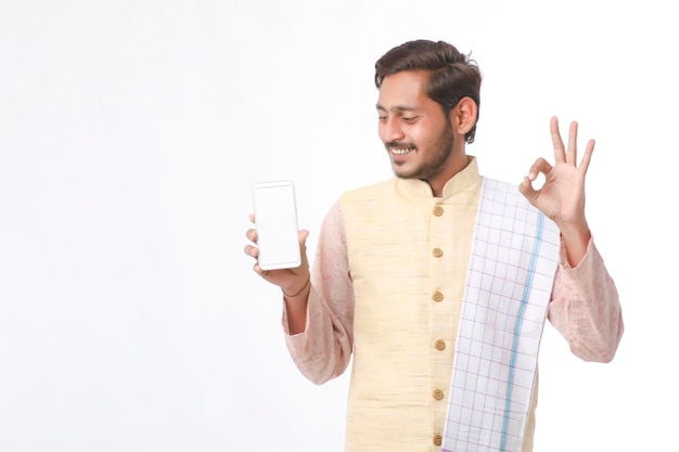 Młody człowiek indyjski w tradycji nosić i pokazując ekran smartfona na białym tle.