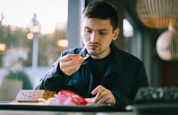 Zdjęcie młody człowiek je fast food w restauracji.