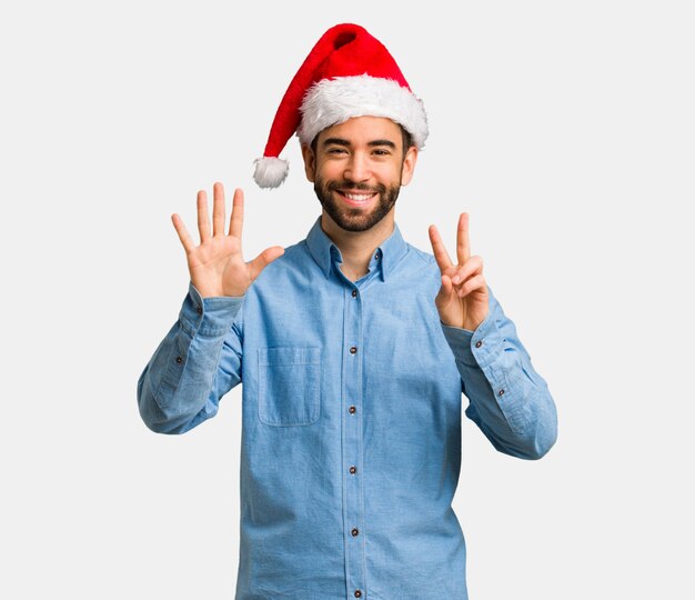 Młody człowiek jest ubranym Santa kapelusz pokazuje liczbę siedem
