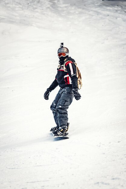 Młody człowiek jeździ na snowboardzie i cieszy się mroźnym zimowym dniem na górskich zboczach.