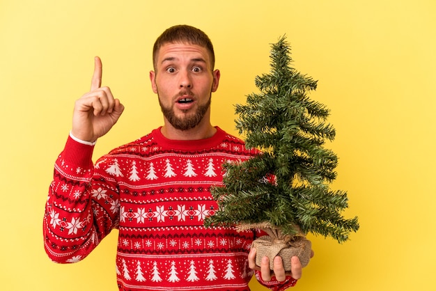 Młody człowiek kaukaski kupowanie drzewka na Boże Narodzenie na białym tle na żółtym tle o pomysł, koncepcja inspiracji.
