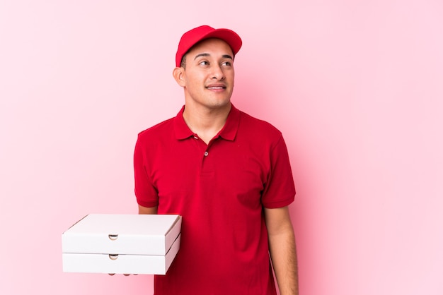 Młody człowiek Łaciński dostawy pizzy na białym tle marzy o osiągnięciu celów i zamierzeń