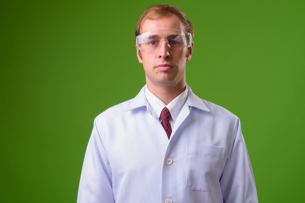 Młody człowiek lekarz w okularach ochronnych przed zieloną ścianą