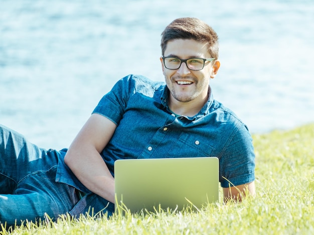 Młody człowiek, leżąc na trawie i za pomocą laptopa