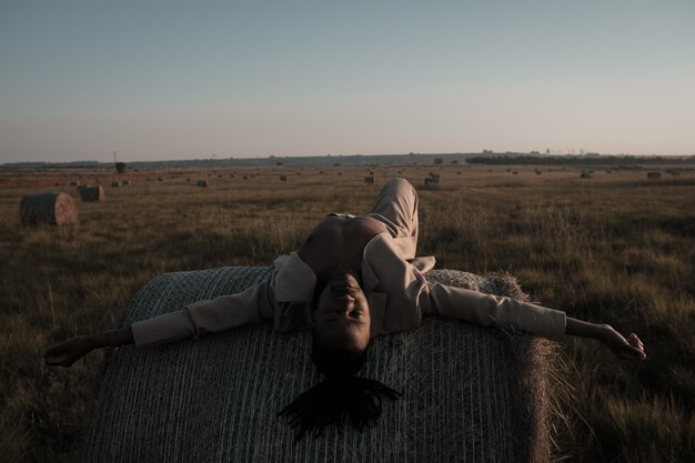 Zdjęcie młody człowiek leżący na bałce siana w krajobrazie rolniczym
