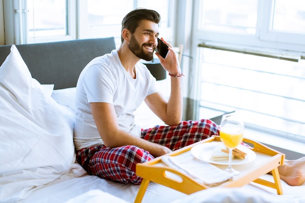 Młody Człowiek Ma śniadanie W łóżku I Używa Telefon Komórkowego