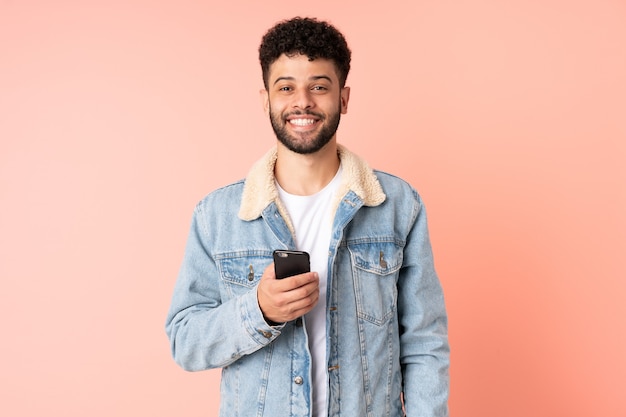 Młody człowiek Maroka za pomocą telefonu komórkowego na białym tle na różowym tle z zaskoczenia wyrazem twarzy