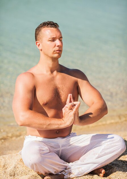 Młody człowiek medytuje na plaży.