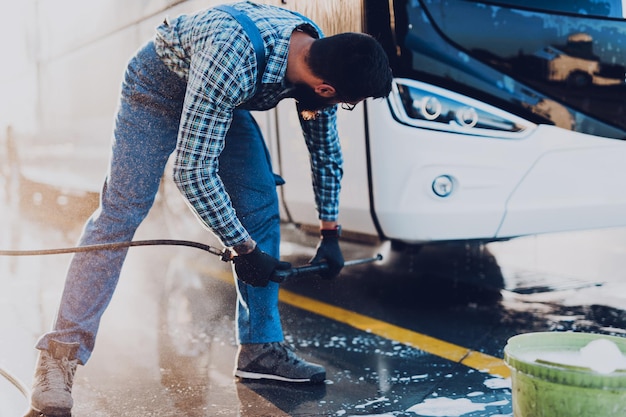 Młody człowiek mycie autobusu wodą pod wysokim ciśnieniem. Selektywne skupienie.