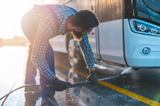 Młody człowiek mycie autobusu wodą pod wysokim ciśnieniem. Selektywne skupienie.