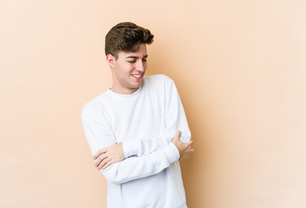 Młody człowiek na białym tle na beżowej ścianie uśmiechnięty pewnie ze skrzyżowanymi rękami