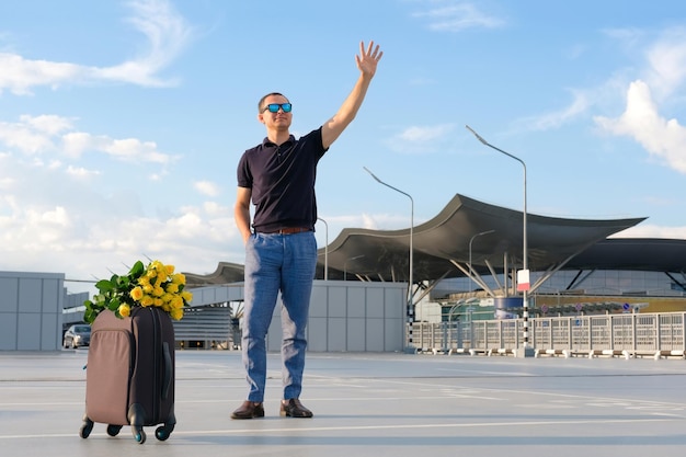 Młody człowiek na parkingu lotniska z bagażem macha do pasażerów Transport w podróży służbowej