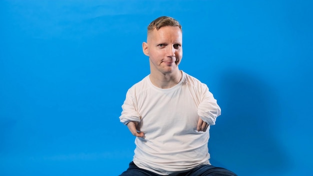 Młody człowiek niepełnosprawny w białej koszulce na niebieskim, odosobnionym tle