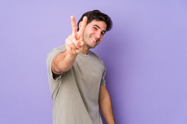 Młody człowiek odizolowany na fioletowej ścianie radosny i beztroski pokazujący palcami symbol pokoju.