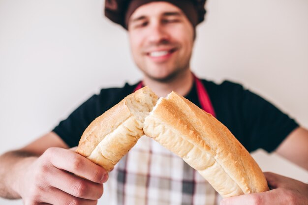 Młody Człowiek Odizolowywający Nad ścianą. Baker Na Białym Tle Na Trzymanie I Chrupanie Tradycyjnych Chlebowych Francuskich Bagietek. Smaczny Pyszny Posiłek.