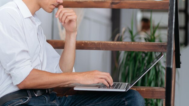 Młody człowiek odpoczywa w swoim domu i za pomocą laptopa