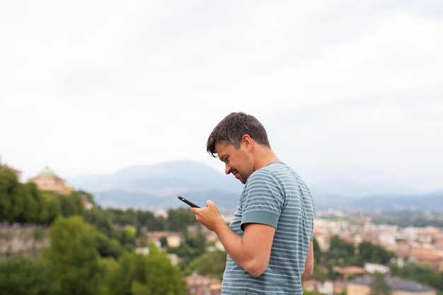 Młody Człowiek Ogląda Surfowanie Po Internecie Wygląda Na Inteligentny Telefon W Mieście. Koncepcja Podróży. Podróżny. Letnie Wakacje.