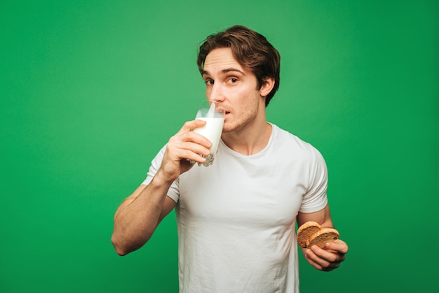 Młody człowiek pić szklankę mleka z ciasteczkami