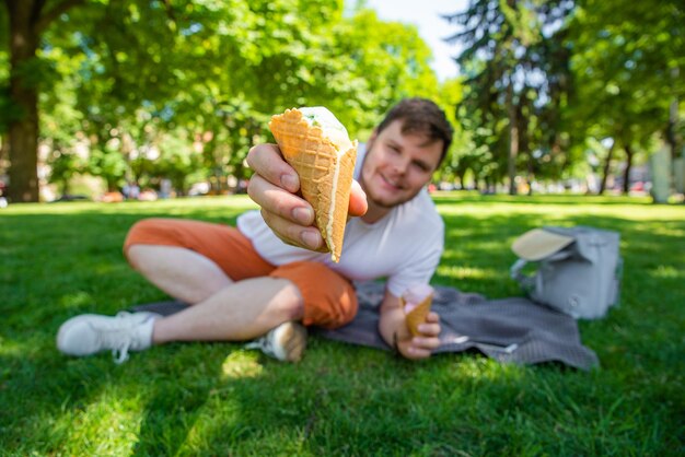 Młody człowiek pokazujący topniejące lody w parku miejskim z bliska szerokiego anioła