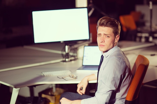 Młody człowiek pracuje na komputerze w nocy w ciemnym biurze. Projektant pracuje w późniejszym czasie.