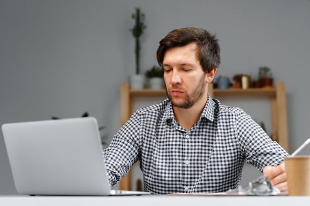 Młody człowiek pracuje na laptopie przy swoim stole roboczym