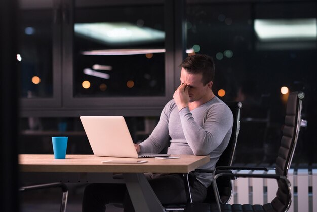 Młody człowiek pracuje na laptopie w nocy w ciemnym biurze. Projektant pracuje w późniejszym czasie.