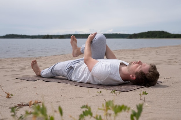 Młody człowiek praktykujący jogę pavanamuktasana na świeżym powietrzu na plaży