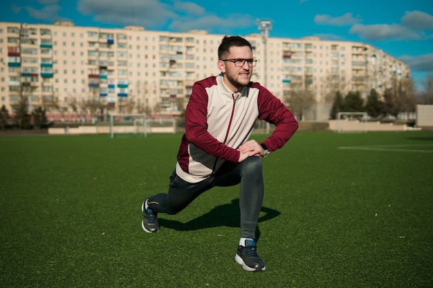 Zdjęcie młody człowiek rozciągający się na stadionie w okularach