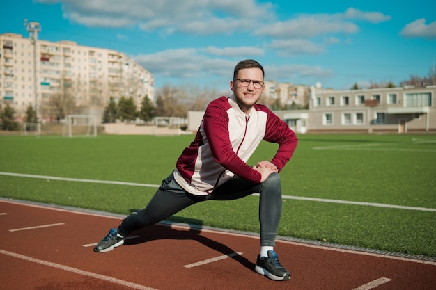 Zdjęcie młody człowiek rozciągający się na stadionie w okularach