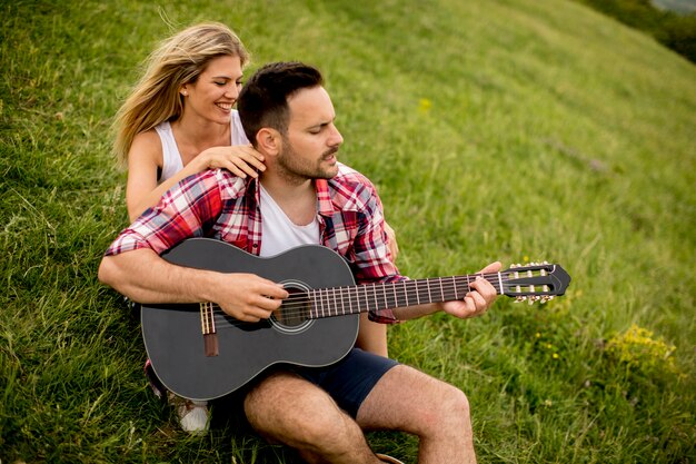 Młody człowiek siedzi na trawie z dziewczyną i gra na gitarze