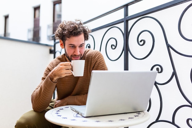 Młody człowiek sprawdzanie poczty elektronicznej na komputerze przenośnym i picie kawy rano. Koncepcja pracy z domu