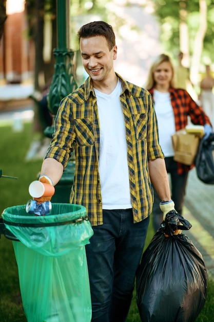 Młody człowiek stawia śmieci w plastikowej torbie w parku, jako wolontariusz