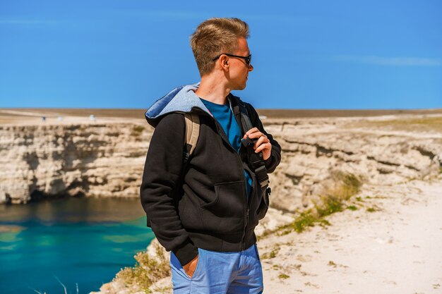 Młody człowiek stoi na wysokim klifie z widokiem na łuki skalistych klifów i turkusową wodę morską