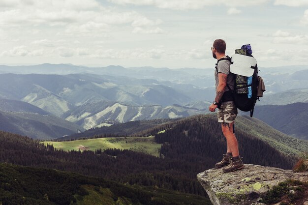 Młody człowiek stojący na szczycie klifu w górach latem z widokiem na przyrodę